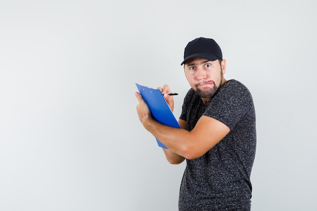 Foto gratuita fattorino in t-shirt e berretto che prende appunti negli appunti e sembra divertente