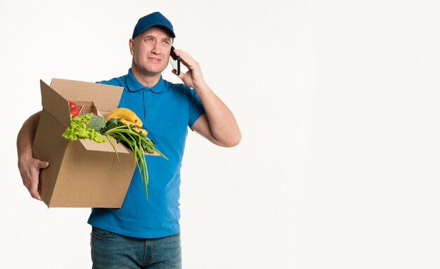 Delivery man talking on phone with grocery box and copy space