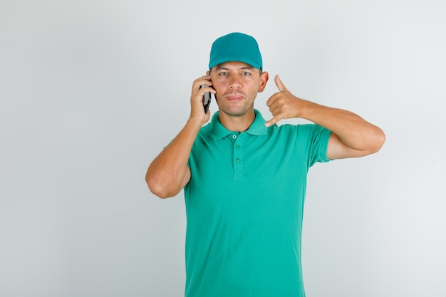 キャップ付きの緑のtシャツを親指で電話で話している配達人