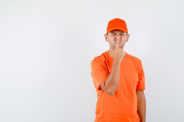 오렌지 티셔츠와 모자에 손가락으로 코를 만지고 우울한 배달 남자