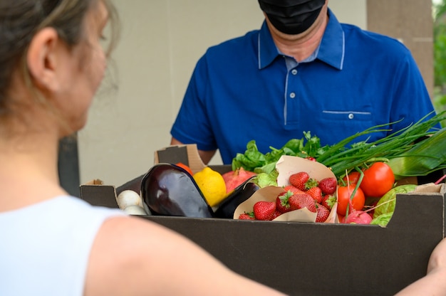 Доставка человек в маске и держит коробку с овощами