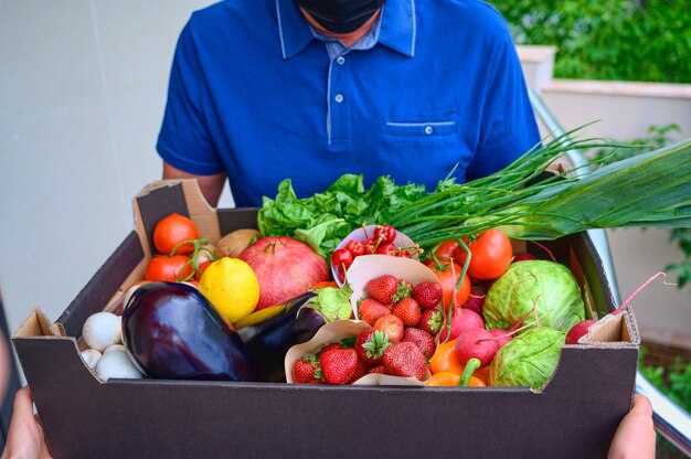 Delivery man wearing a face mask and holding a box with vegetables