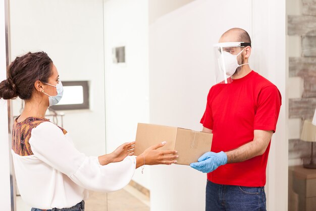 Delivery man wearing protection giving female costumer her order.
