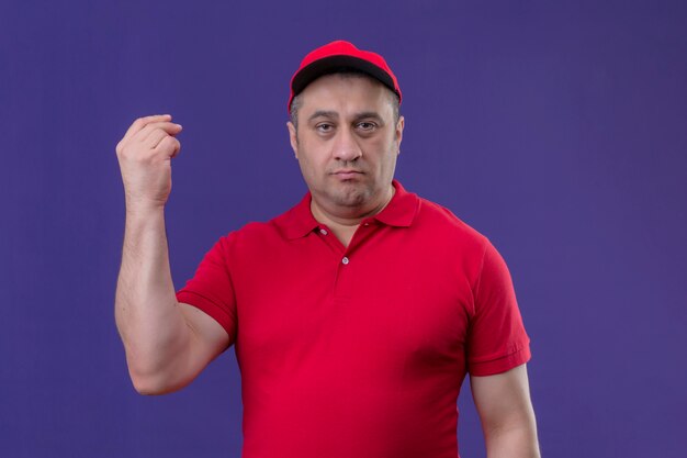 Доставщик в красной форме и кепке недоволен поднятой рукой над изолированной фиолетовой стеной
