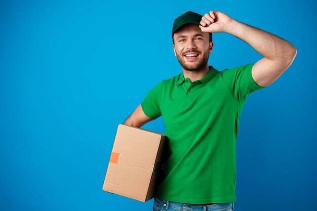 Delivery man with box in studio against blue background