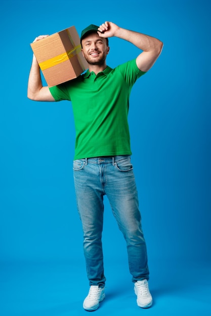 Delivery man with box in studio against blue background