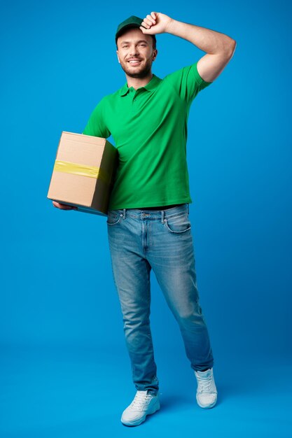 Delivery man with box in studio against blue background