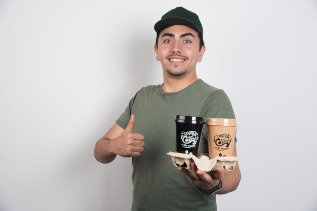 Delivery man with cups of coffees making thumbs up on white background.