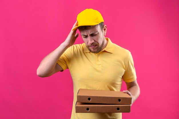 黄色のポロシャツとピザの箱を手で立っているミスの配達人は間違いのための頭の上に手で立ってエラーを忘れた分離ピンクの悪い記憶概念を忘れた
