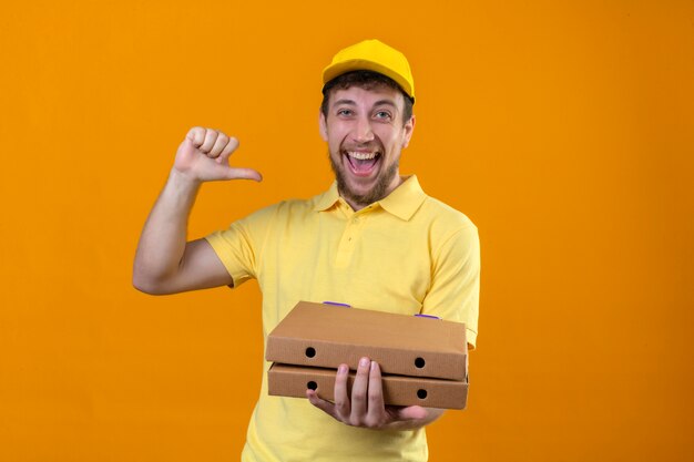 delivery man in yellow polo shirt and cap pointing to himself looking confident self-satisfied smiling cheerful standing on isolated orange