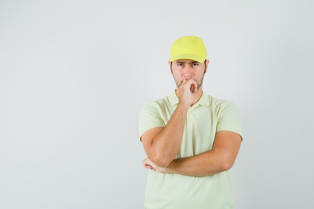 Delivery man in yellow uniform standing in thinking pose and looking hesitant , front view.