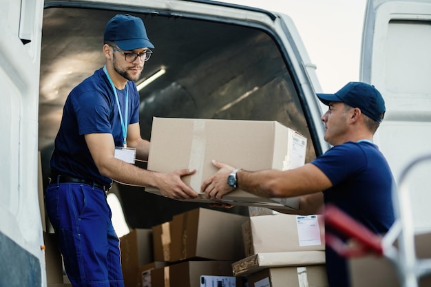 Free photo delivery men loading carboard boxes in a van while getting ready for the shipment