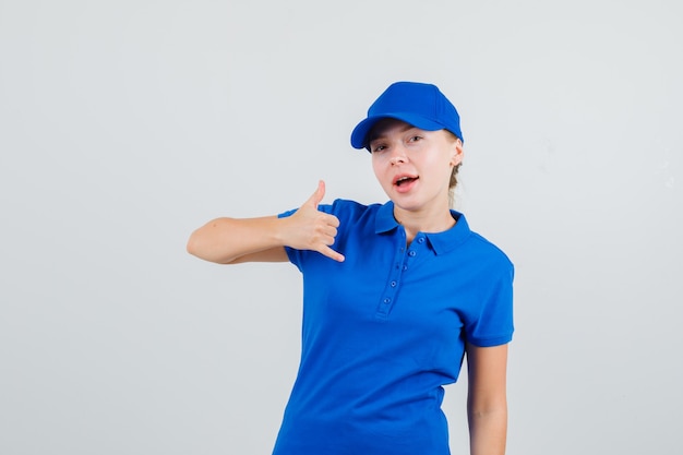 Delivery woman in blue t-shirt and cap showing phone gesture and looking confident