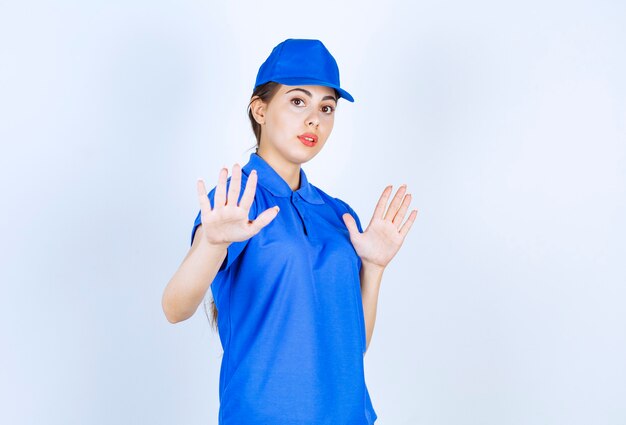 Delivery woman employee in blue uniform standing and showing stop sign .
