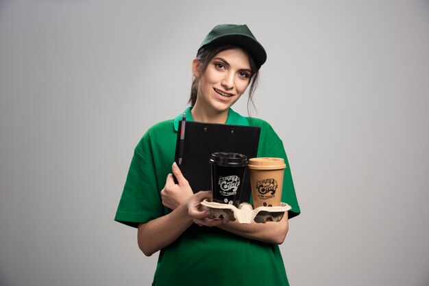 クリップボードとコーヒーカップを保持している緑の制服を着た出産の女性。