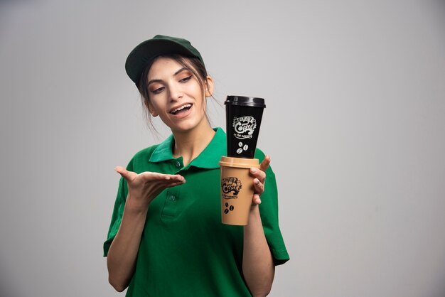 Delivery woman in green uniform holding coffee cups