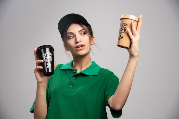 Delivery woman in green uniform looking at coffee cups