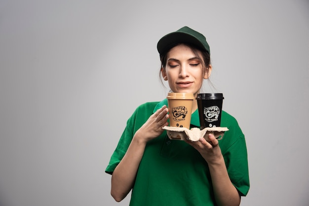 Delivery woman in green uniform posing with cups of coffee. 