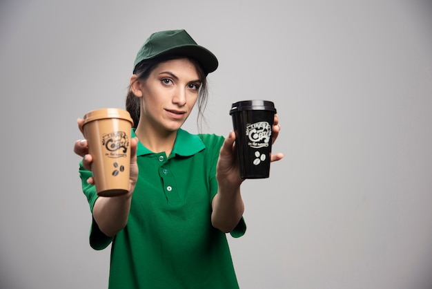Доставка женщина в зеленой форме позирует с вкусным кофе.