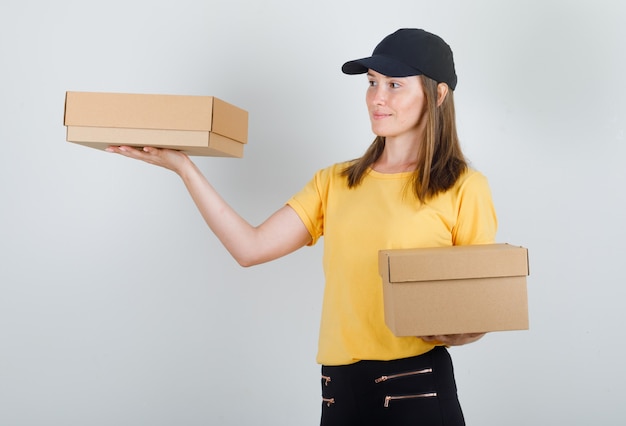 Delivery woman holding cardboard boxes in t-shirt, pants and cap