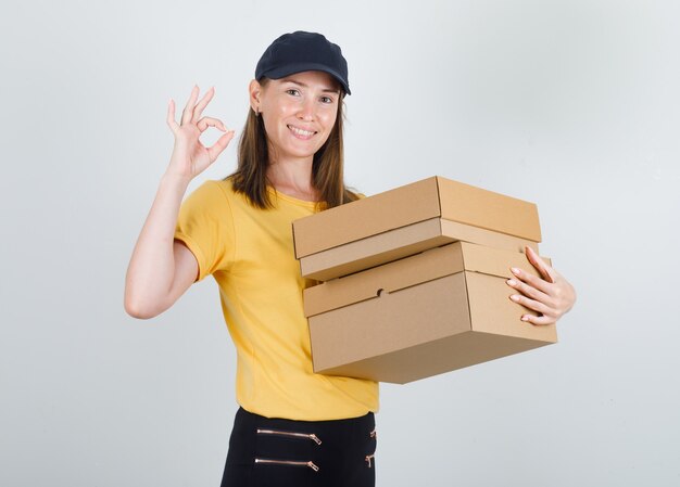 Delivery woman holding cardboard boxes with ok sign in t-shirt