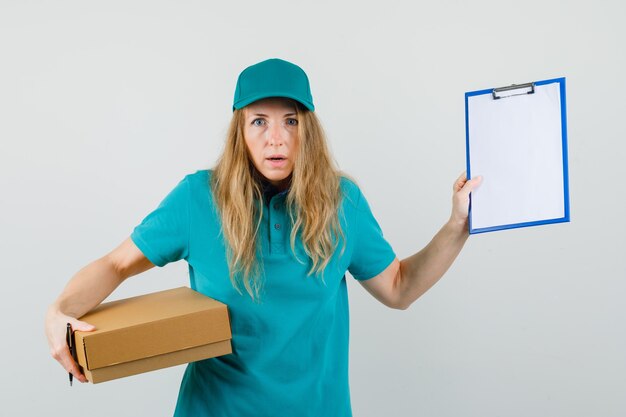 Delivery woman holding clipboard and cardboard box in t-shirt, cap and looking puzzled. 