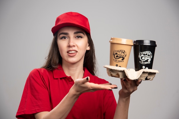 Free photo delivery woman holding coffee cups on gray wall.