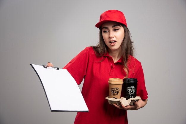 Delivery woman holding coffee cups and looking at clipboard. 