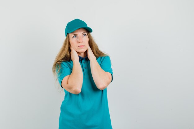 Delivery woman holding hands on neck in t-shirt, cap and looking pensive. 