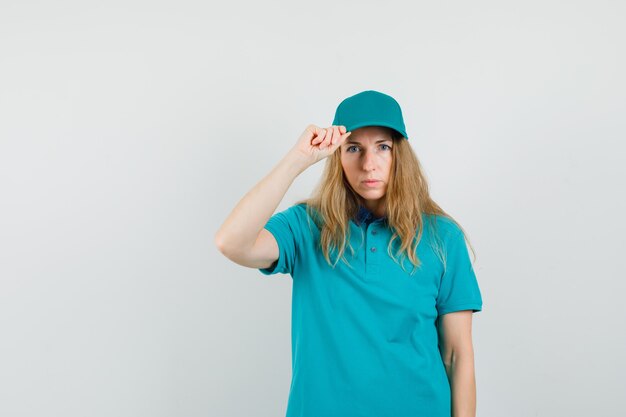 Delivery woman holding his cap in t-shirt, cap and looking serious 