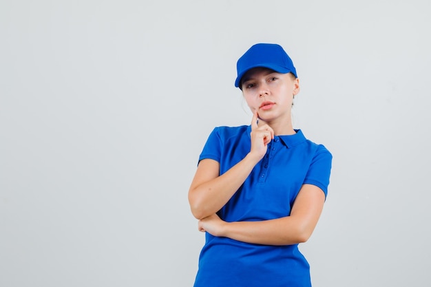 Женщина-доставщик смотрит в синюю футболку и кепку и выглядит задумчиво