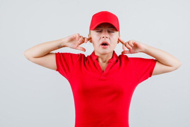 赤いTシャツとキャップで指で耳を塞いでイライラしている分娩女性