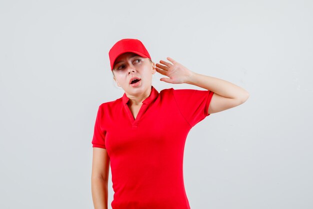 Delivery woman raising arm in protective manner in red t-shirt and cap and looking scared