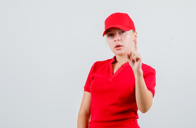 Delivery woman in red t-shirt and cap pointing up and looking pensive