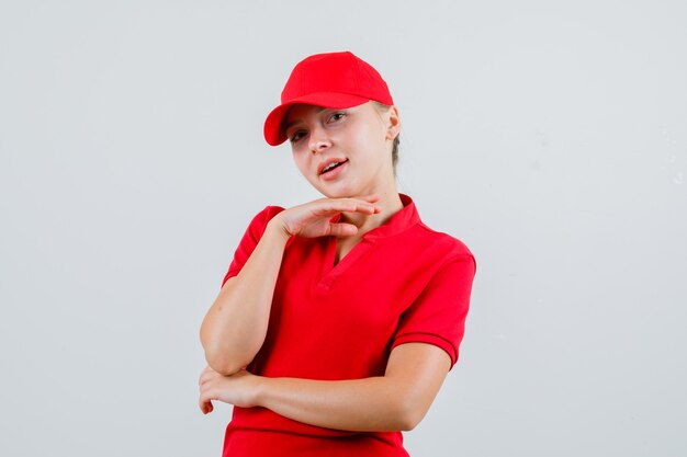 Женщина-доставщик в красной футболке и кепке подпирает подбородок на поднятой руке и выглядит мило
