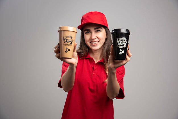 delivery woman in red uniform holding coffee cups. 