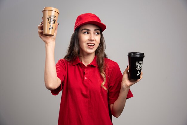 커피 컵을 들고 빨간 제복을 입은 배달 여자.