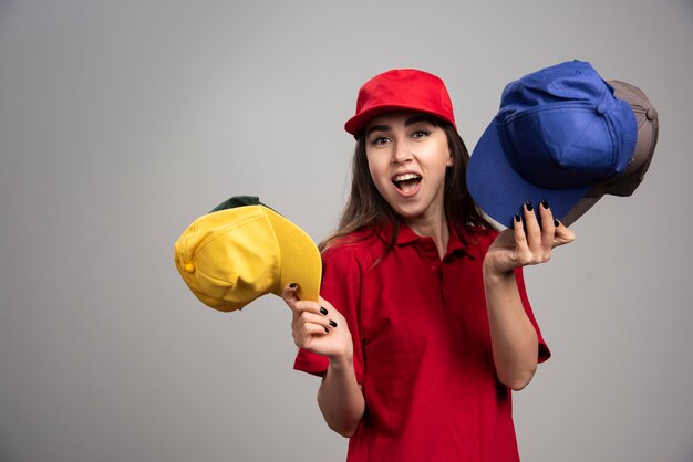 Delivery woman in red uniform holding colorful caps. 