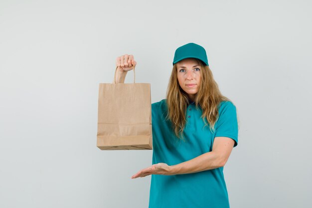 Delivery woman showing paper bag in t-shirt, cap 