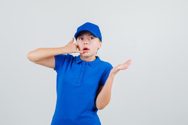 Delivery woman showing phone gesture with spread palm in blue t-shirt and cap