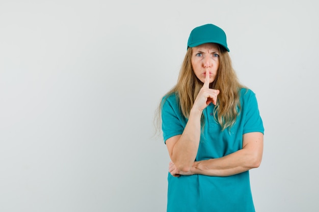 Delivery woman showing silence gesture while frowning in t-shirt, cap and looking serious. 