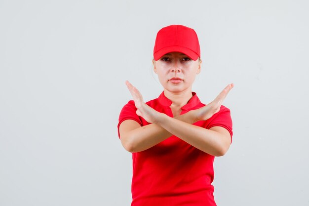 Free photo delivery woman showing stop gesture in red t-shirt and cap and looking strict