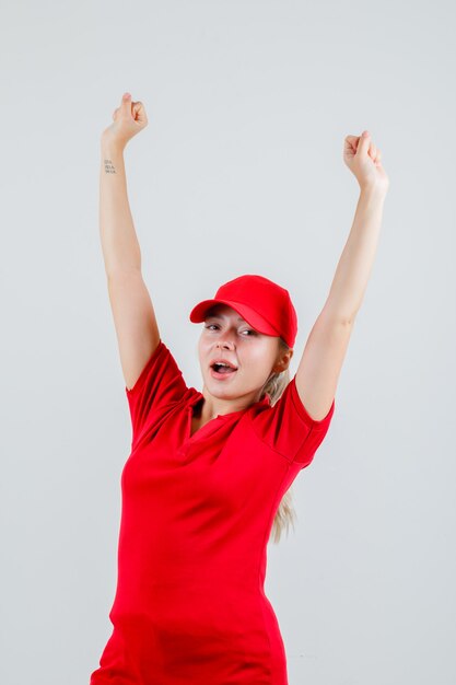 赤いTシャツとキャップで勝者のジェスチャーを示し、幸せそうに見える配達の女性