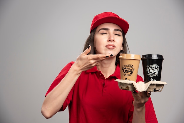 Delivery woman smells coffee cups. 