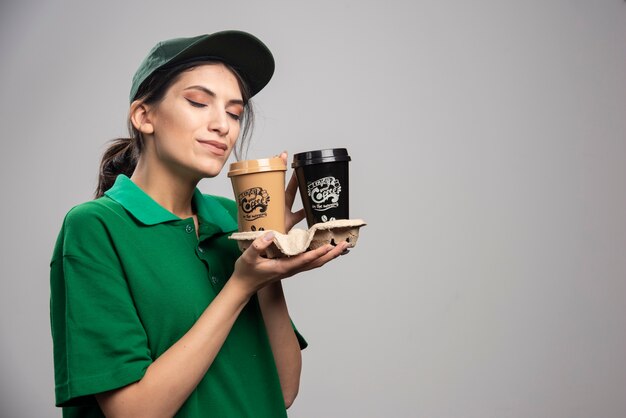 Delivery woman smells cups of coffee. 