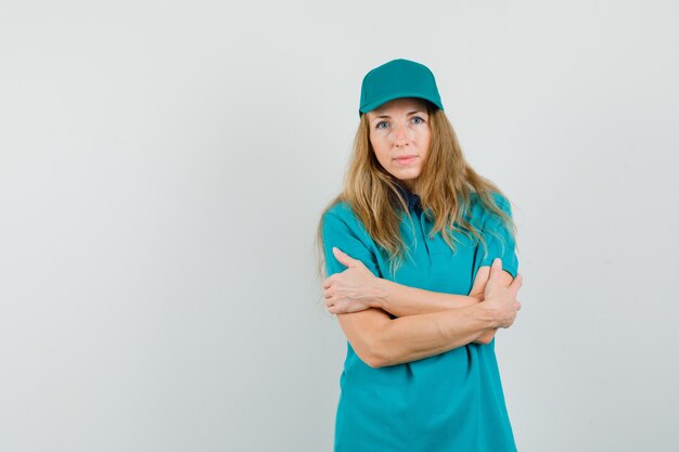 Delivery woman standing with crossed arms in t-shirt, cap and looking confident. 