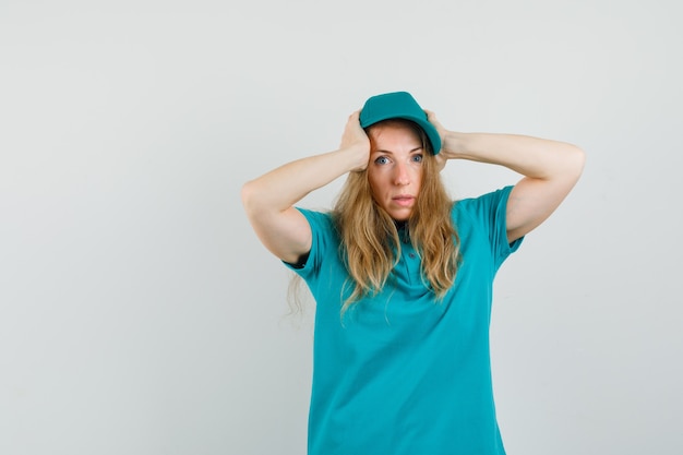 Delivery woman in t-shirt, cap clasping head in hands and looking puzzled 