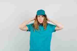 Free photo delivery woman in t-shirt, cap holding hands to head and looking tired