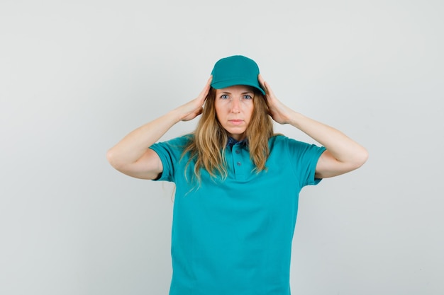 Delivery woman in t-shirt, cap holding hands to head and looking tired 