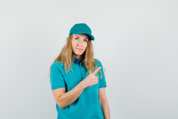 Delivery woman in t-shirt, cap pointing away and looking confident 